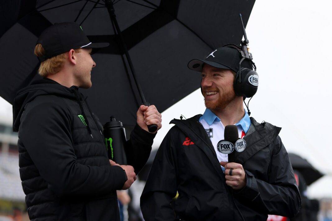 CONCORD, NORTH CAROLINA - MAY 27: Ty Gibbs, driver of the #19 He Gets Us Toyota,(L) is interviewed by NASCAR Cup Series driver, Tyler Reddick on the grid under an umbrella prior to the NASCAR Xfinity Series Alsco Uniforms 300 at Charlotte Motor Speedway on May 27, 2023 in Concord, North Carolina